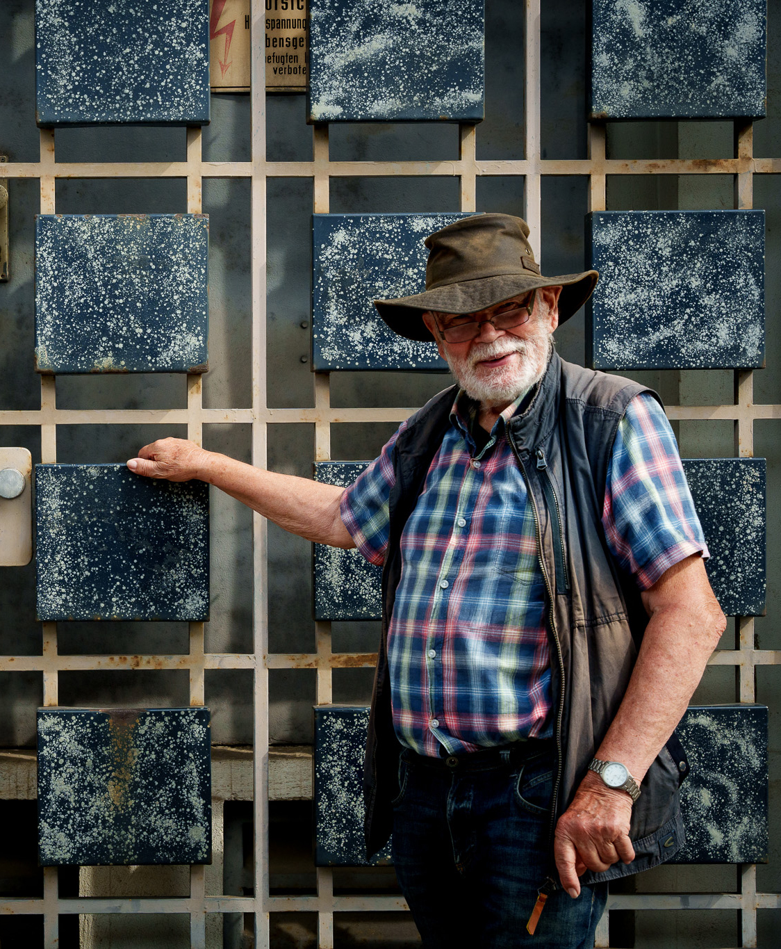 Ein Foto, das Wolfgang Kärgel vor einer der von ihm gestalteten Türen mit den charakteristischen Emaille-Kacheln zeigt